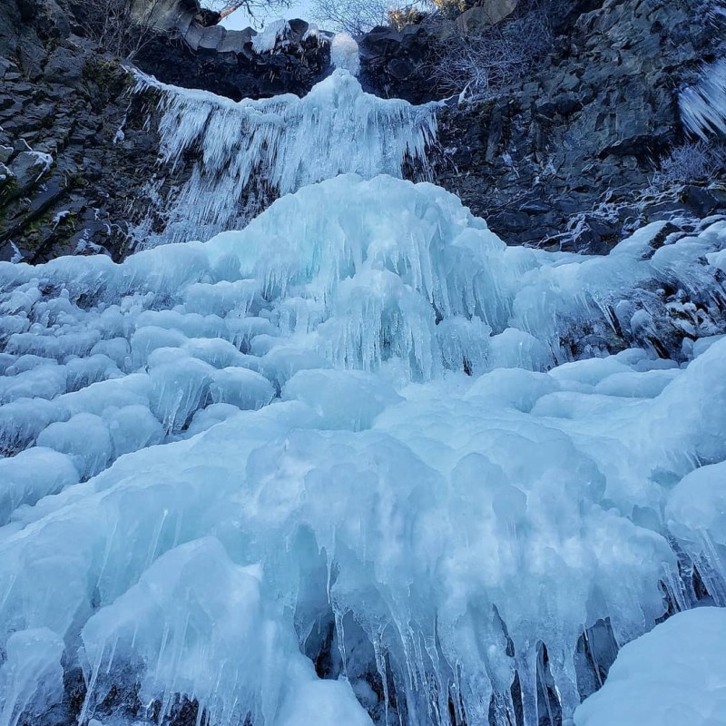 a waterfall with trees on the side of a snow covered mountain