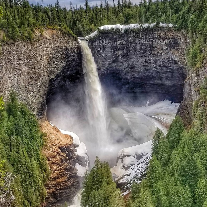 a large waterfall over some water with Wells Gray Provincial Park in the background
