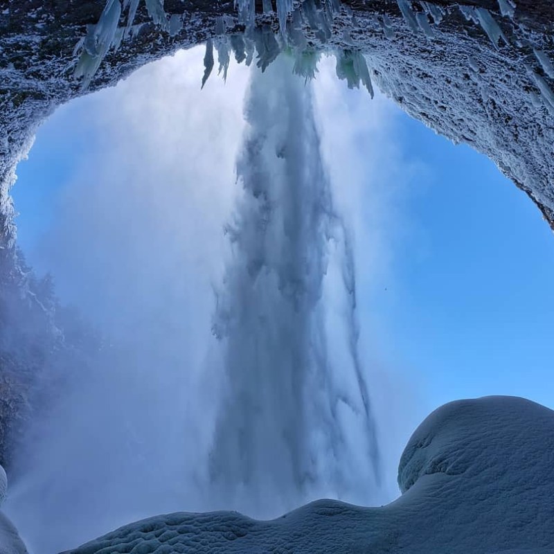 a waterfall with trees on the side of a snow covered mountain