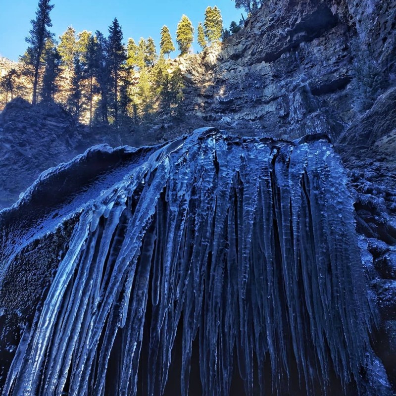 a waterfall with trees on the side of a snow covered mountain