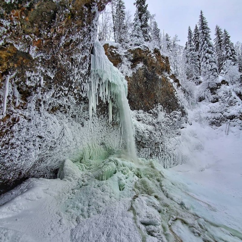 a waterfall with trees on the side of a snow covered slope