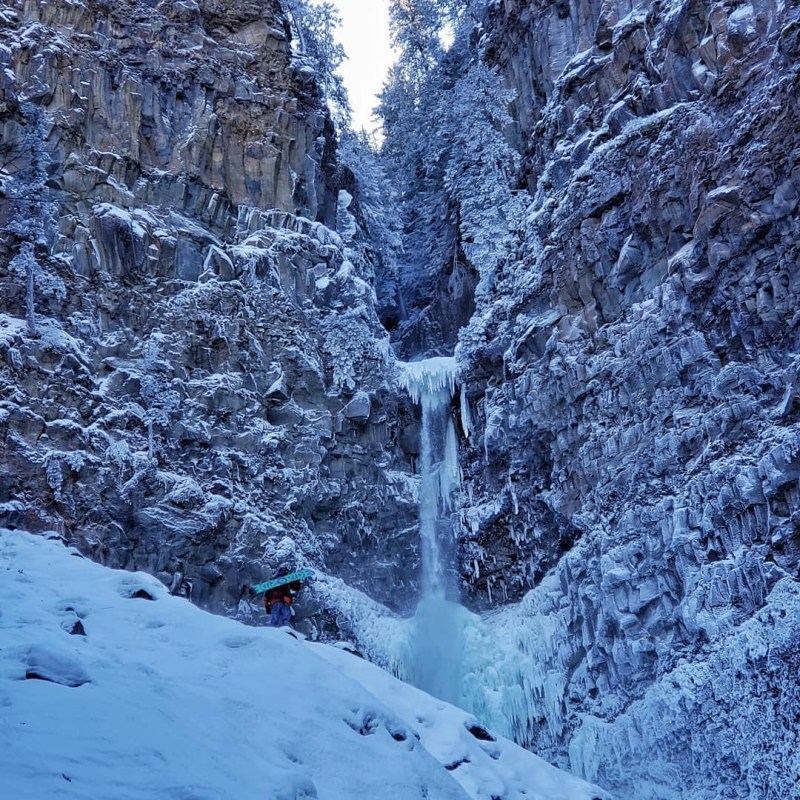 a waterfall with trees on the side of a snow covered slope