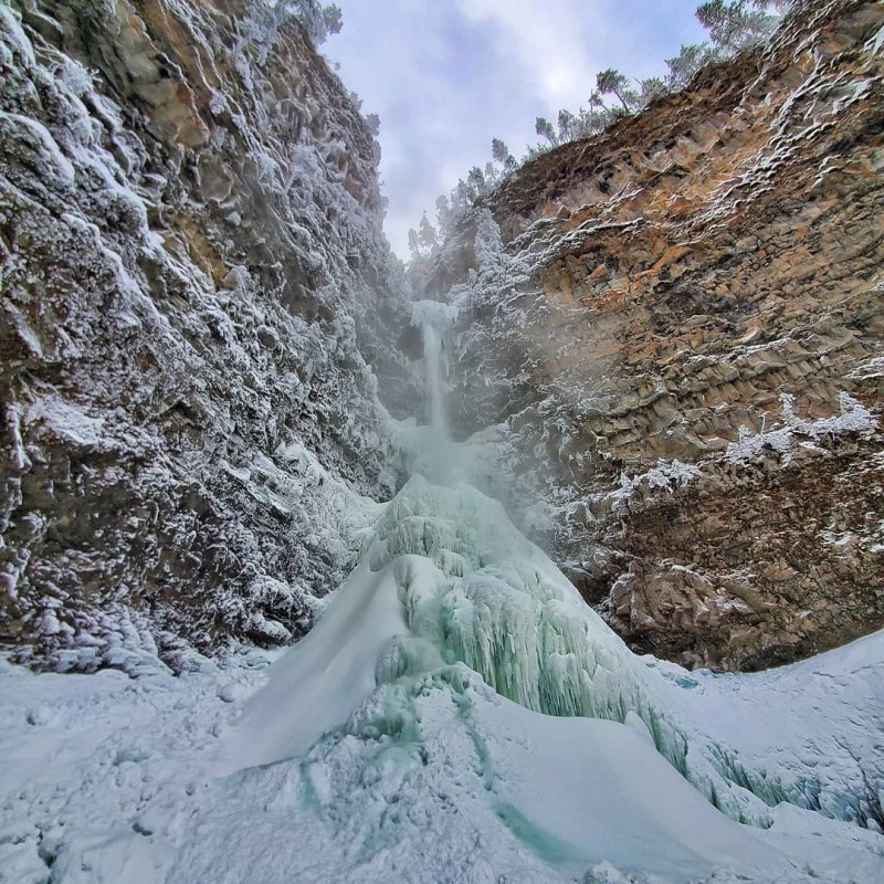 a waterfall with trees on the side of a snow covered mountain