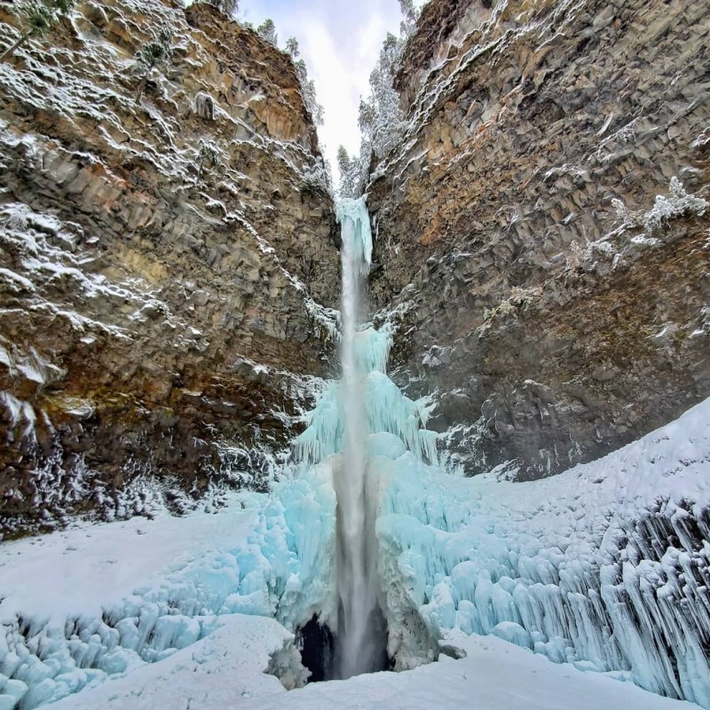 a waterfall with trees on the side of a snow covered mountain