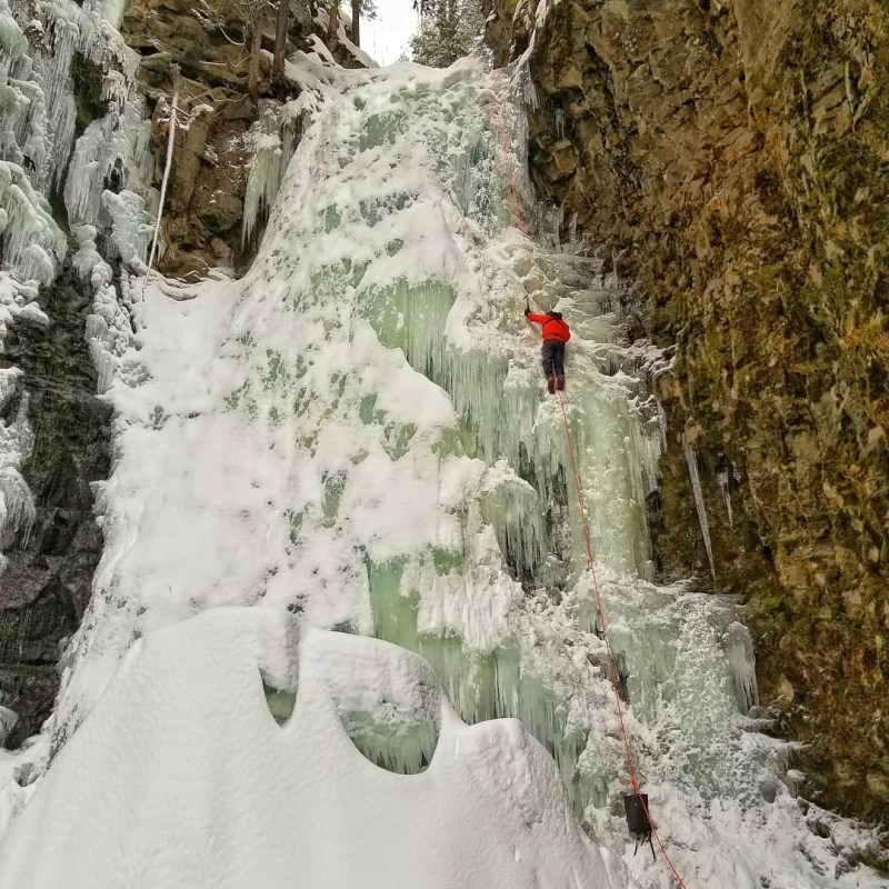 a waterfall with trees on the side of a snow covered slope