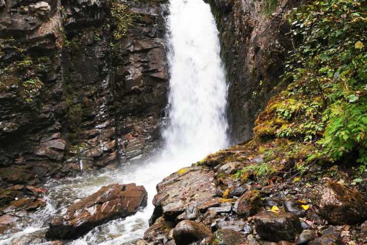 A tall waterfall flows between rocky cliffs surrounded by lush greenery.