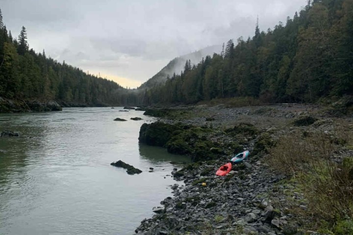 River with rocky shore, two kayaks, and forested hills under cloudy sky