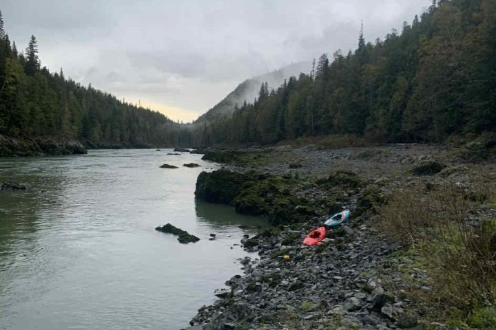 River with rocky shore, kayaks, and forested hills under a cloudy sky.