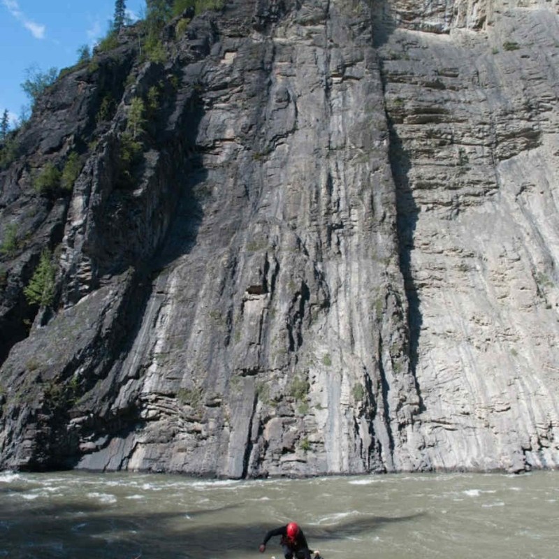 People prepare rafts by a large cliff and river.