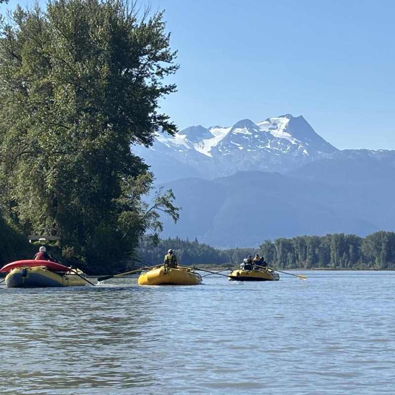 Three yellow rafts on a river with mountains and trees in the background.