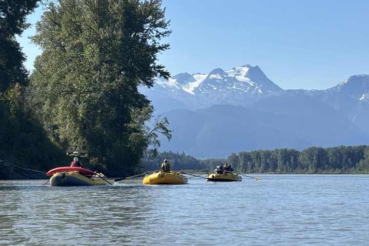 Three rafts on a river with mountains and trees in the background.