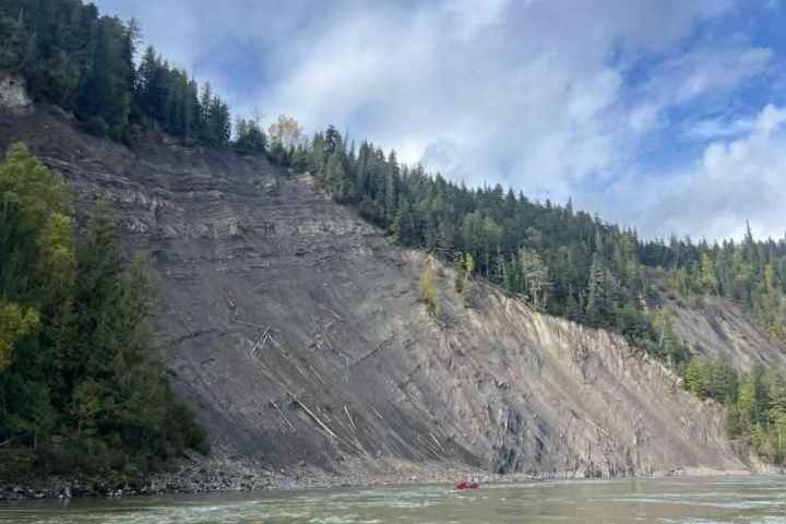 Steep forested hillside beside a river under a cloudy sky.