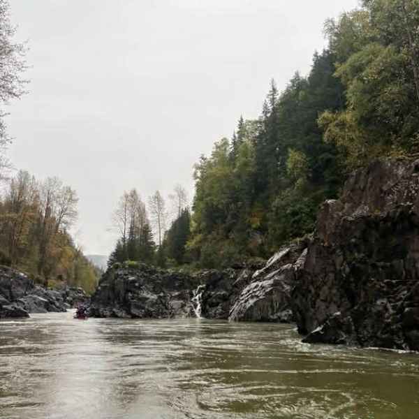River flowing between rocky cliffs with trees on a cloudy day.