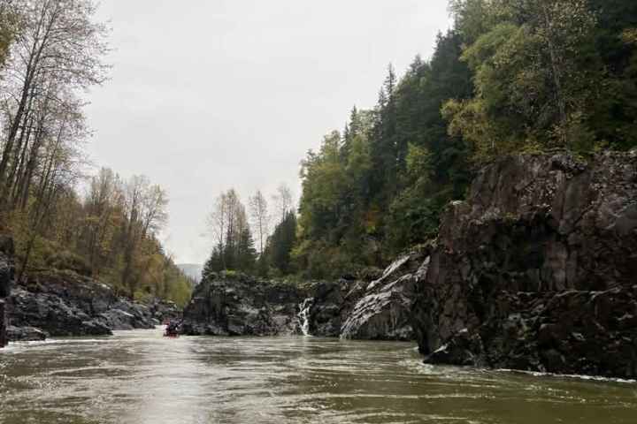 Calm river flowing between rocky cliffs with trees on a cloudy day.