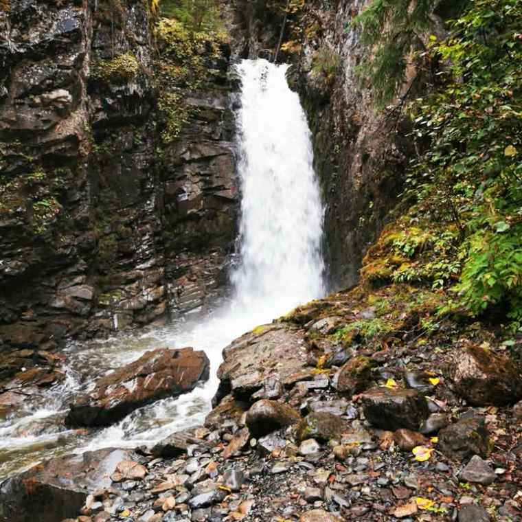 Waterfall flowing between rocky cliffs surrounded by green foliage.