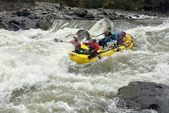 People whitewater rafting on a river with rocks and trees in the background.