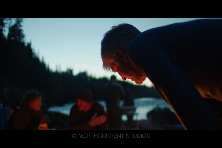 People gathered outdoors near a lake at dusk, conversing.