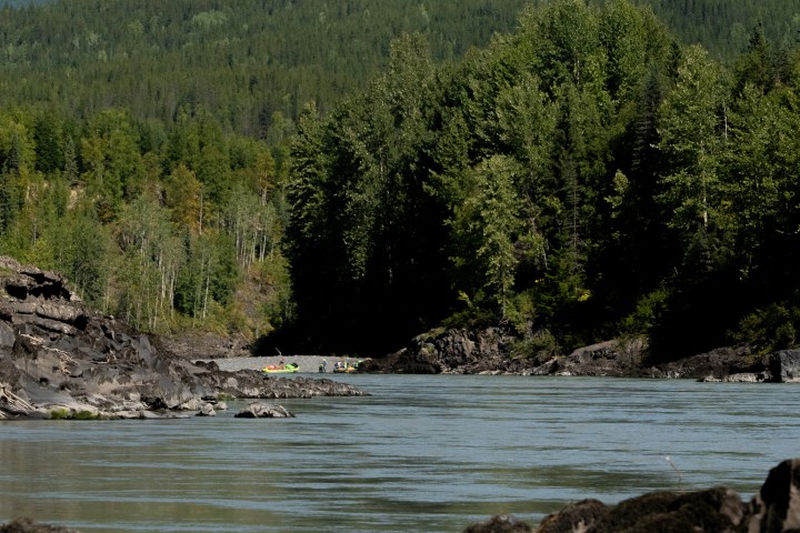 Scenic river view with rocky banks and forested mountains in the background.
