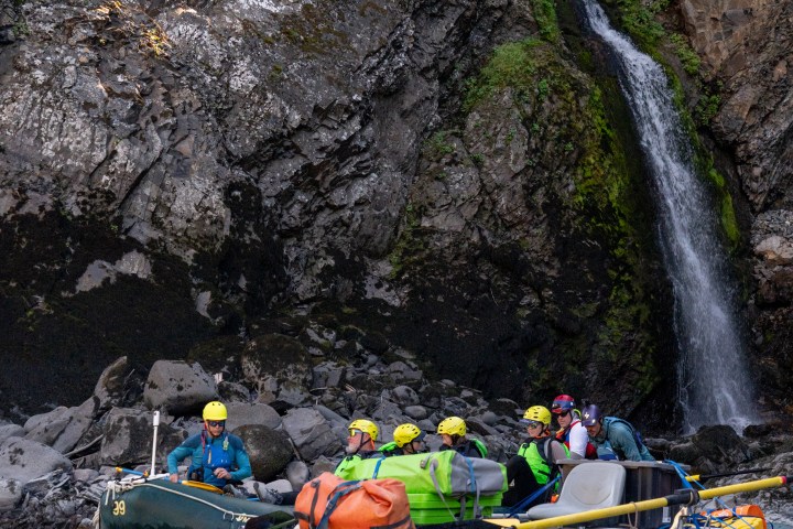 Rafts with people near a waterfall in a rocky gorge.